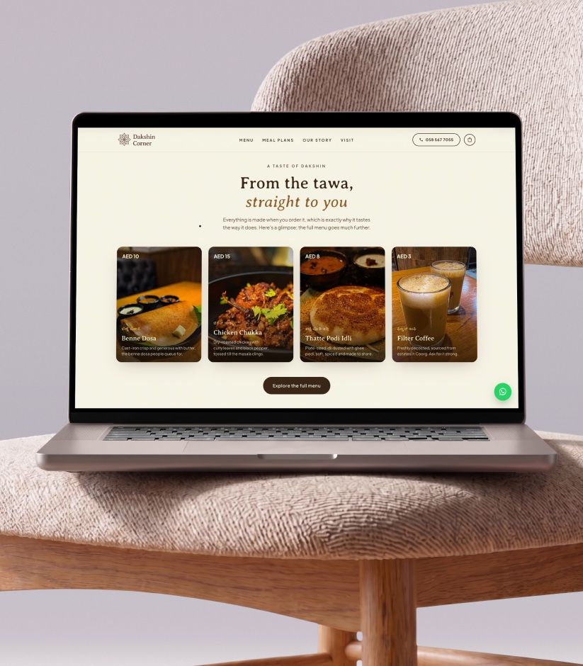 Dakshin Corner's website on a laptop on a woven chair: From the Tawa, Straight to You, above four dishes.
