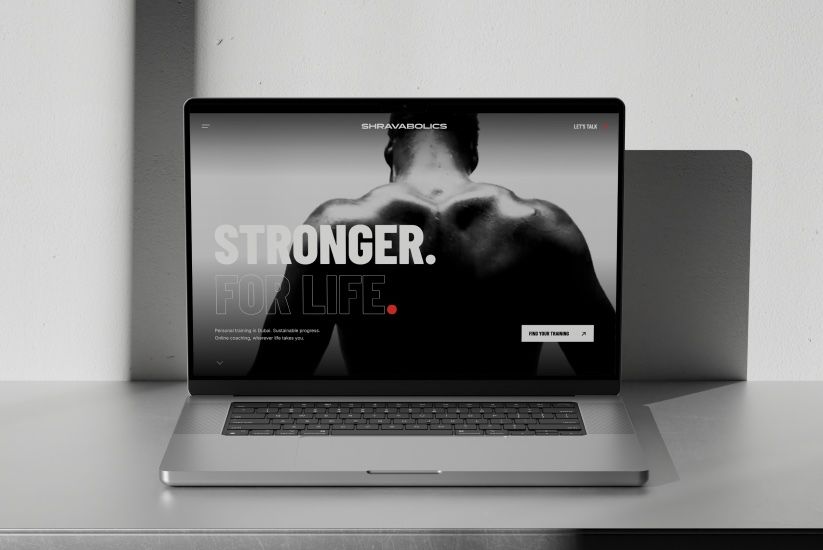 The Shravabolics website on a laptop against a pale wall: a black and white back shot of an athlete under the line Stronger. For Life.